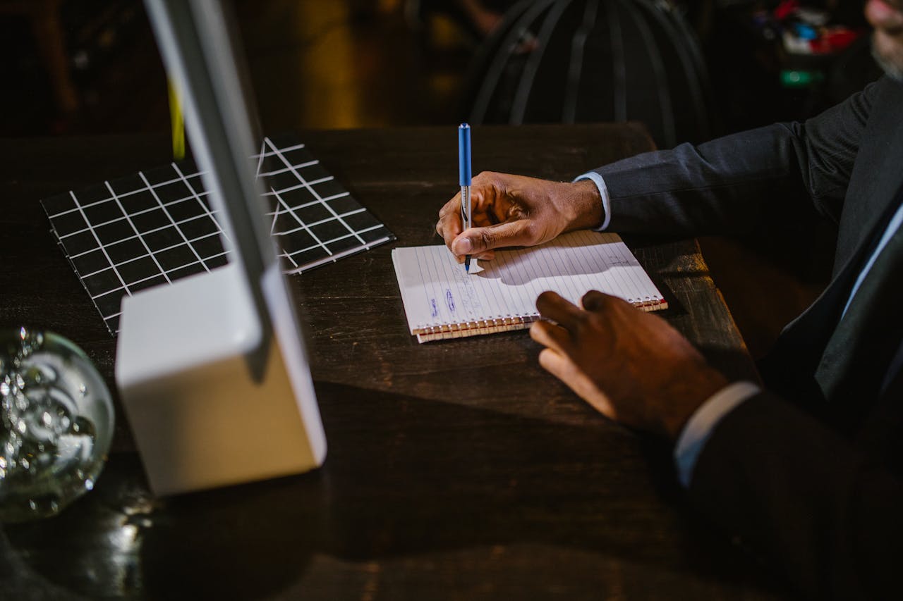 why-choose-me-01 A businessman in a suit writing notes on a notebook at a desk, suggesting a professional office environment.
