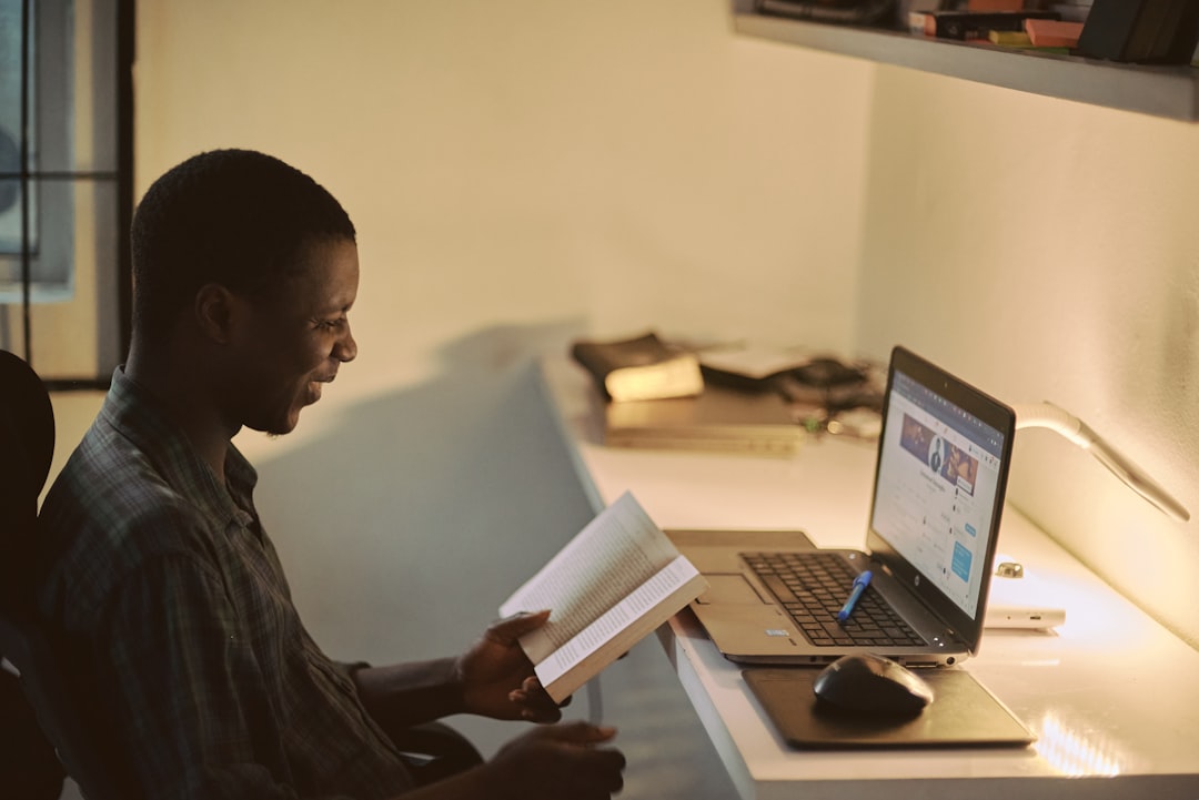 gallery-04 Portrait of a creative happy African man taking a break from work to enjoy reading a book, his workspace blurred in the background
